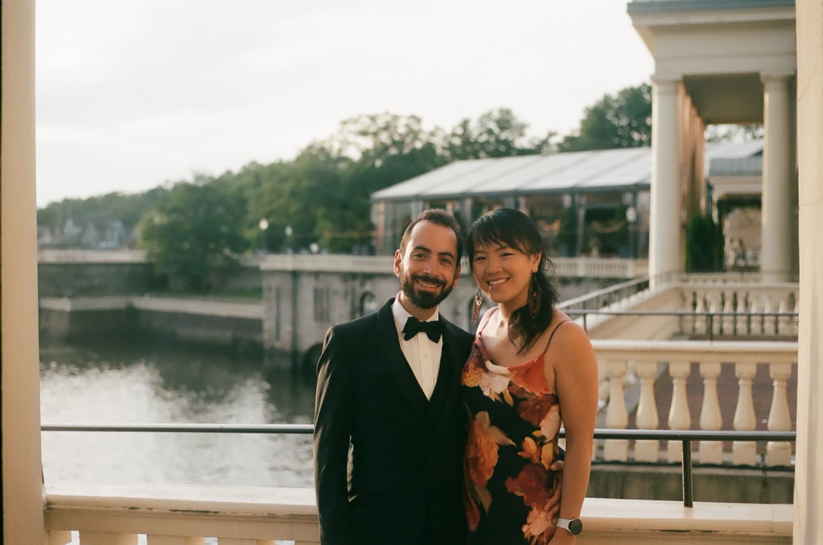 Jason Edelstein in a tuxedo, smiling on a waterfront balcony beside his partner.